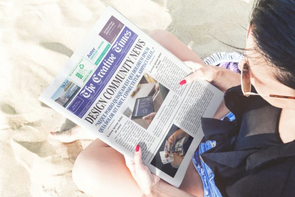 海滩场景新闻报纸印刷设计图样机 Girl Reading Newspaper Beach Scene Mockup